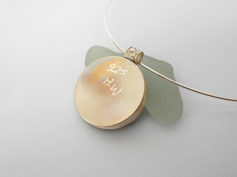 May include: A silver pendant necklace with a round, engraved disc. The disc has the inscription "H.W. 8.25" on it.