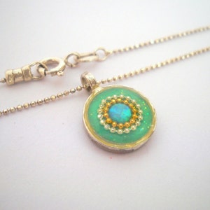 May include: A silver chain necklace with a round pendant featuring a green background, gold and white beads, and a blue opal in the center.