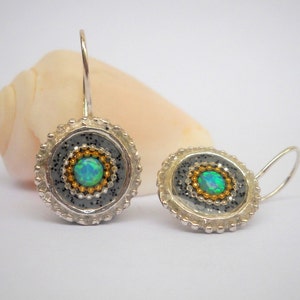 May include: A pair of silver earrings with a round, gray, and gold design. Each earring features a small, green opal gemstone in the center.