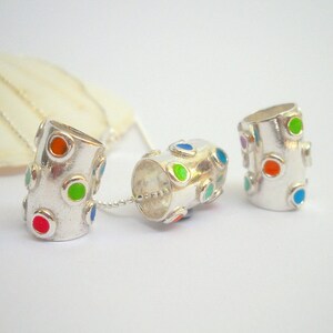 May include: Three silver pendant charms with colorful enamel dots. The charms are cylindrical and have a smooth, polished finish.