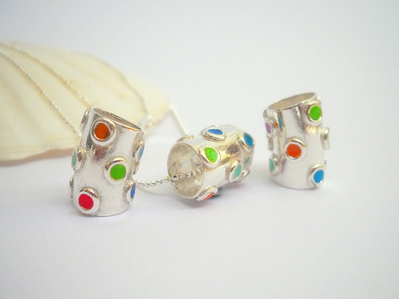 May include: Three silver pendant charms with colorful enamel dots. The charms are cylindrical and have a smooth, polished finish.