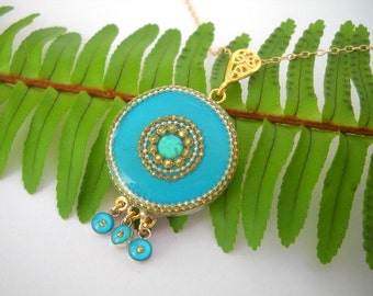 May include: A turquoise blue pendant necklace with a gold filigree design and a small opal gemstone in the center. The pendant is surrounded by a gold beaded border and has three small turquoise blue beads hanging from the bottom.