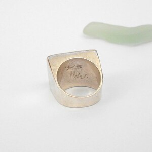 May include: A silver ring with a square top and a rounded band. The inside of the band is stamped with "925 Hilv".