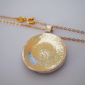 May include: A silver pendant necklace with a round, hammered silver pendant. The pendant has a small inscription on the back that reads "925". The necklace is attached to a gold chain.