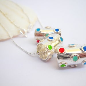 May include: Three silver cylinder-shaped pendants with colorful dots. The pendants are on a silver chain.