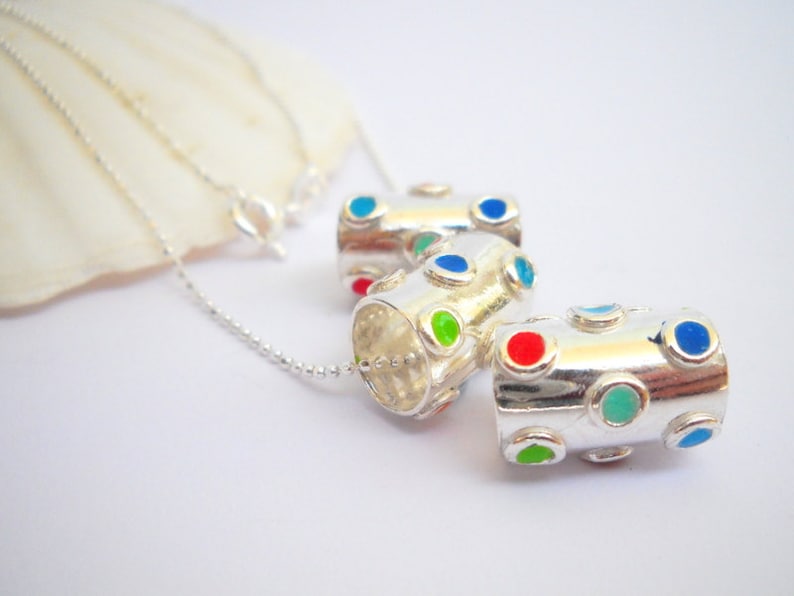 May include: Three silver cylinder-shaped pendants with colorful dots. The pendants are on a silver chain.