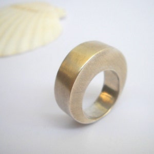 May include: A silver ring with a rounded, smooth, and slightly curved design. The ring is made of metal and has a polished finish.
