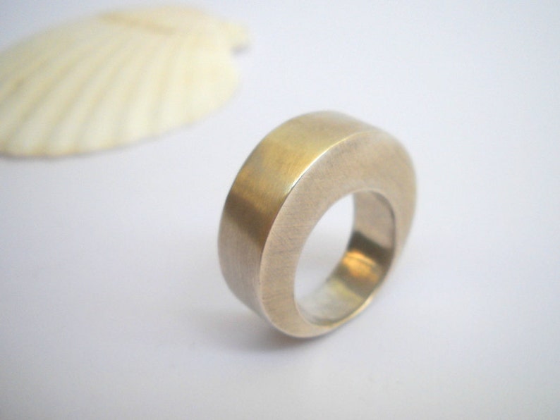 May include: A silver ring with a rounded, smooth, and slightly curved design. The ring is made of metal and has a polished finish.