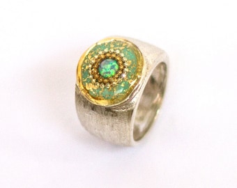 May include: A silver ring with a green and gold circular setting featuring a small iridescent opal gemstone.