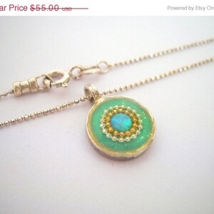 May include: A silver chain necklace with a green pendant featuring a blue opal surrounded by gold and white beads.