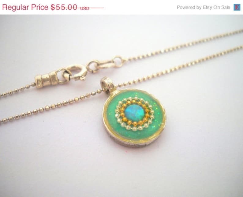 May include: A silver chain necklace with a green pendant featuring a blue opal surrounded by gold and white beads.