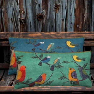 Peut inclure: Deux coussins rectangulaires décorés de motifs d'oiseaux. Le coussin arrière est bleu et le coussin avant est vert. Les deux présentent divers oiseaux colorés perchés sur des branches, notamment des oiseaux jaunes, rouges, bleus et orange.