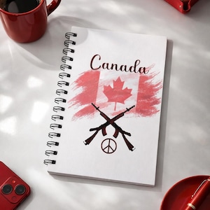 Può includere: Un taccuino a spirale bianco con la scritta "Canada" e un disegno della bandiera canadese. Il disegno include fucili incrociati e un simbolo di pace. Sono visibili anche una tazza, un telefono, un vassoio e una penna rossi.