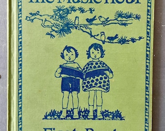 May include: A vintage children's book titled "The Music Hour First Book." The cover is light green with blue text and illustrations, including two children and a branch with birds. The book has a decorative border.