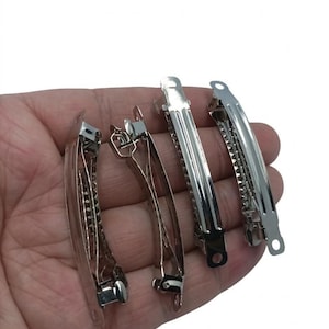 May include: Several silver metal hair clips are displayed. The clips have a curved design and a hinged clasp. The image shows a variety of styles, all in a shiny silver finish, suitable for various hairstyles.