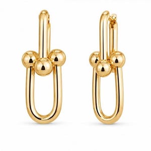 May include: A pair of gold-toned earrings featuring a vertical U-shaped link design. Each earring consists of a smooth, elongated oval loop connected to a horizontal bar adorned with three polished spherical beads at the front, creating a link effect.