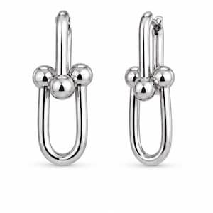 May include: A pair of silver-toned hoop earrings featuring a polished U-shaped link design. Each earring is accented with three smooth, spherical beads positioned horizontally across the centre of the elongated metal loop, creating a balanced look.