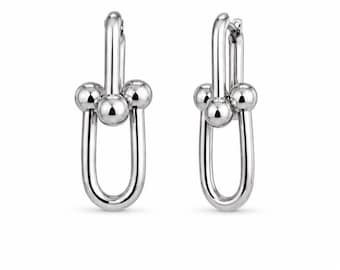 Könnte beinhalten: Ein Paar silberfarbene Creolen mit einem polierten U-förmigen Glieddesign. Jeder Ohrring ist mit drei glatten, kugelförmigen Perlen akzentuiert, die horizontal über der Mitte der länglichen Metallschlaufe positioniert sind und für einen ausgewogenen Look sorgen.