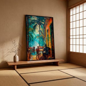 Puede incluir: Una impresi&oacute;n art&iacute;stica enmarcada que representa una vibrante escena de caf&eacute; al aire libre con palmeras y una figura sentada a una mesa. La obra de arte presenta una colorida paleta de azules, verdes y naranjas, creando una atm&oacute;sfera tropical. La impresi&oacute;n se exhibe en una plataforma de madera.