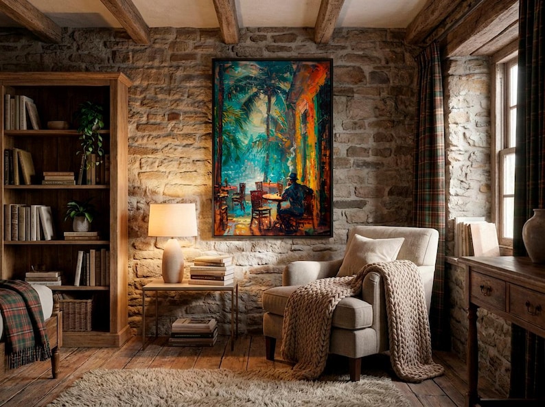 Puede incluir: Un sal&oacute;n acogedor con una pared de piedra, vigas de madera y una estanter&iacute;a. Una pintura de una escena de caf&eacute; cuelga sobre un sill&oacute;n beige con una manta de punto. Una l&aacute;mpara est&aacute; sobre una mesa auxiliar.