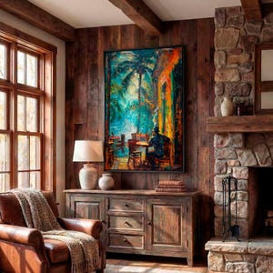 Puede incluir: Una pintura al &oacute;leo que representa una escena de caf&eacute; con una persona sentada a una mesa bajo palmeras. La obra de arte cuelga sobre un mueble de madera con cajones y puertas. Un sill&oacute;n de cuero con una manta est&aacute; cerca de una ventana.