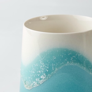 May include: A ceramic mug with a gradient design, transitioning from white to a vibrant turquoise blue. The mug features a textured, crystalline band where the colors meet, adding a unique visual element.