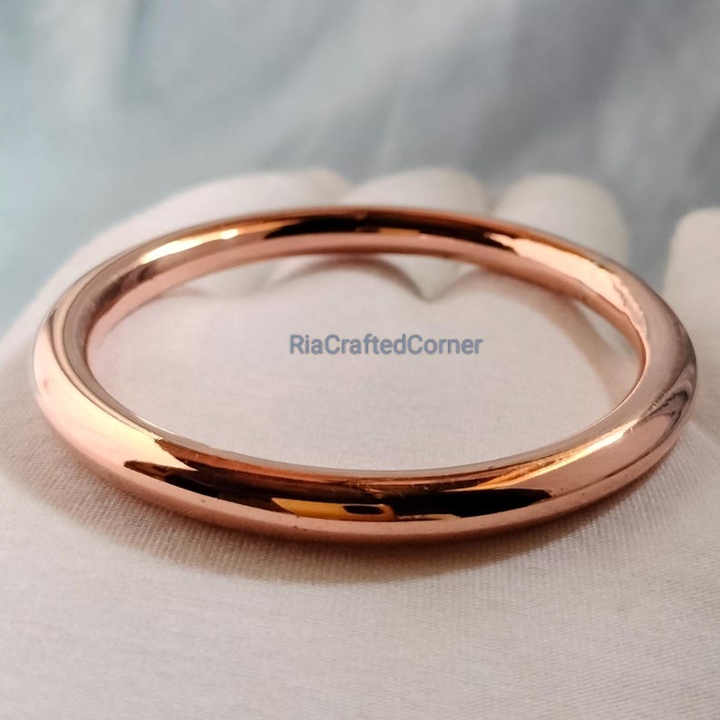May include: A rose gold bangle bracelet with a smooth, polished finish. The circular bracelet is displayed on a white surface. The text "RiaCraftedCorner" is visible in the image.