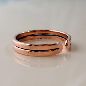 Può includere: Un anello regolabile in oro rosa con un design a doppia fascia. L'anello ha una finitura liscia e lucida e un piccolo spazio su un lato per la regolazione. L'anello è progettato per essere indossato su un dito o un dito del piede.