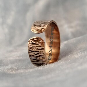 Puede incluir: Anillo abierto dorado con superficie texturizada. El anillo presenta un dise&ntilde;o org&aacute;nico con una textura similar a la corteza. El dise&ntilde;o abierto permite el ajuste de tama&ntilde;o. El texto "RiaCraftedCorner" es visible en el lateral del anillo.