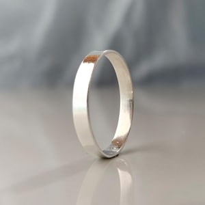 Könnte beinhalten: Ein polierter Silberring mit flachem Band. Der Ring reflektiert das Licht und zeigt seine glatte, glänzende Oberfläche. Der Ring ist ein schlichtes, elegantes Schmuckstück.
