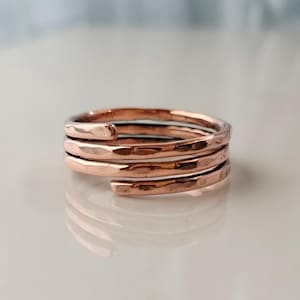 May include: A rose gold ring with a hammered texture. The ring wraps around the finger multiple times, creating a layered effect. The metal has a warm, reflective sheen, and the design is simple yet elegant.