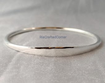 May include: A silver bangle bracelet with a smooth, polished finish. The bracelet is circular and appears to be made of metal. The text "RiaCraftedCorner" is visible on the bracelet. The bangle is displayed on a light-colored, textured surface.