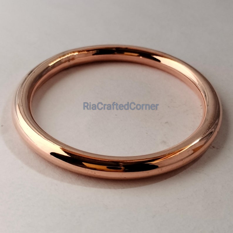 May include: A rose gold metal ring with a smooth, polished surface. The ring is circular and appears to be a solid band. The text "RiaCraftedCorner" is visible on the surface.
