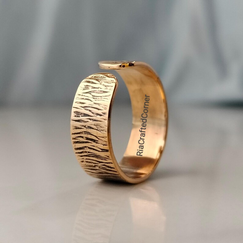 Puede incluir: Un anillo ajustable de color dorado con una superficie texturizada. El anillo tiene un dise&ntilde;o &uacute;nico y el texto "RiaCraftedCorner" es visible en el interior del anillo.