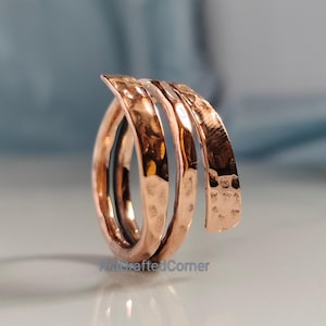 May include: A hammered copper ring with a spiral design. The ring has a textured surface and a warm, reddish-brown colour. The ring is a unique piece of jewellery.