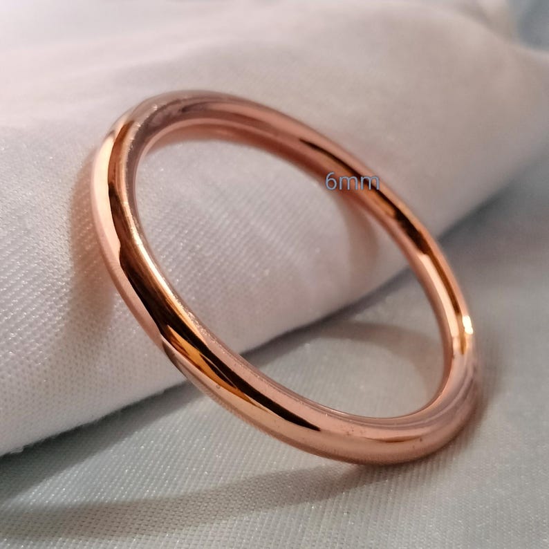 May include: A rose gold ring with a smooth, polished surface. The ring is 6mm wide and has a circular shape. The ring is set against a white and light blue background.