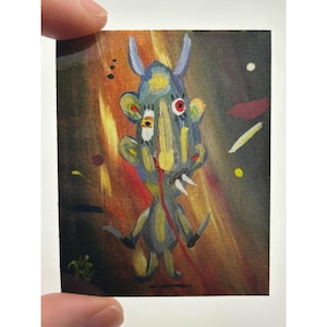 May include: A small, abstract painting of a creature with horns, fangs, and a single red eye. The artwork features a mix of colors, including blue, yellow, and red, with a dark background and abstract shapes.