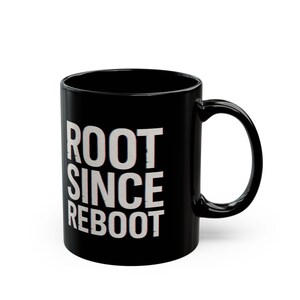 May include: Black ceramic mug featuring the white text "ROOT SINCE REBOOT". The mug has a curved handle and a glossy finish. Suitable for hot or cold drinks, this mug is a simple, everyday item.