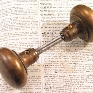 May include: Antique brass doorknob with a classic, rounded design. The doorknob is attached to a metal rod, and is set against the backdrop of an open book.