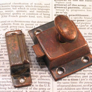 May include: Two antique bronze-colored latches. One is a rectangular catch with a curved handle, and the other is a matching rectangular piece. The latches are likely for a cabinet or small door.