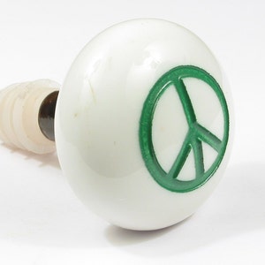 May include: White ceramic bottle stopper with a green peace sign.