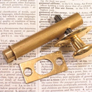 May include: A brass barrel bolt latch featuring a cylindrical sliding bolt with a knob handle and a rectangular strike plate. The hardware has a polished metallic finish and is shown with the bolt mechanism partially extended from its housing.