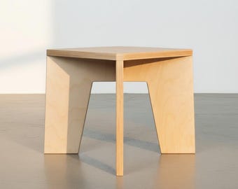 Puede incluir: Una mesa auxiliar de madera clara con una superficie cuadrada y tres patas inclinadas. La mesa está fabricada en madera contrachapada con vetas visibles, presentando un diseño geométrico limpio con una superficie lisa y plana.