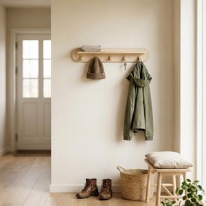 Puede incluir: Un perchero de pared de madera con ganchos, que sostiene una chaqueta verde, un gorro marrón y llaves. Debajo, una cesta tejida, un taburete de madera con un cojín y botas de cuero marrón completan la decoración de la entrada.