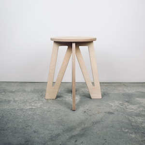 May include: A light-coloured wooden stool with a round seat and a geometric base. The base features angled legs connected by a central support. The stool is approximately 46 cm tall.