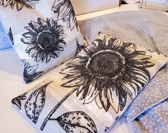 May include: Two white fabric pillow covers with black sunflower designs. The pillows are on a gray and white polka dot fabric.