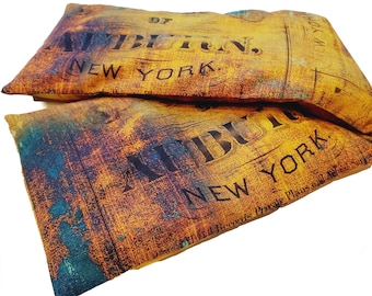 Puede incluir: Dos almohadas de tela amarilla y naranja con el texto "SEBULAN, NEW YORK" impreso en ellas. Las almohadas tienen un aspecto desgastado y vintage.