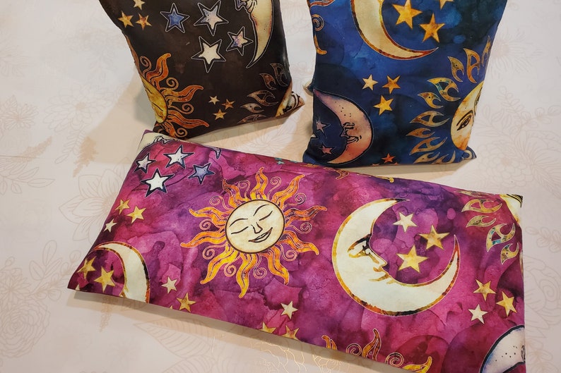 May include: Three decorative pillows with a celestial theme. The pillows are made of fabric with a purple, blue, and black background. The pillows feature a sun, moon, and stars design.