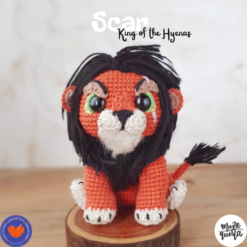 K&ouml;nnte beinhalten: Geh&auml;kelte L&ouml;wenpuppe in Orange, Schwarz und Wei&szlig; mit gr&uuml;nen Augen. &Uuml;ber der Puppe steht der Text "Scar King of the Hyenas". Die Puppe sitzt auf einem Holzsockel. Die Puppe ist handgefertigt.
