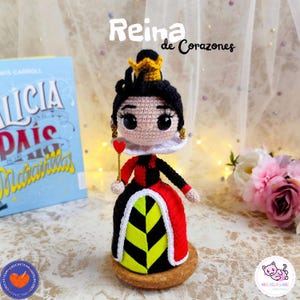 K&ouml;nnte beinhalten: Handgefertigte H&auml;kelpuppe der Herzk&ouml;nigin aus Alice im Wunderland. Die Puppe hat ein schwarz-rotes Kleid, eine goldene Krone und h&auml;lt ein herzf&ouml;rmiges Zepter. Der Text "Reina de Corazones" ist &uuml;ber der Puppe zu sehen.